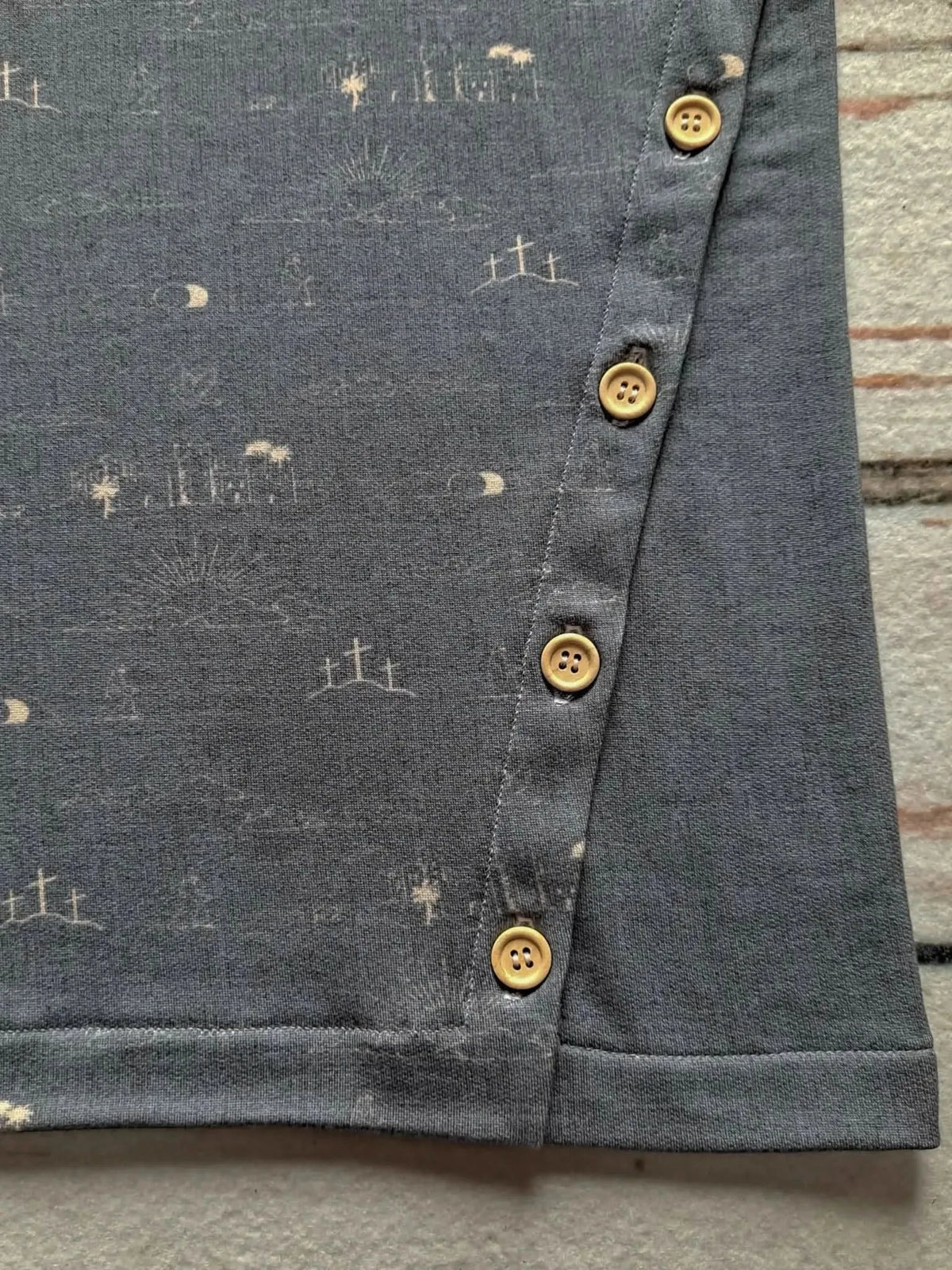 Gray fabric with subtle sky blue print of crosses and moons, featuring yellow buttons along the edge.