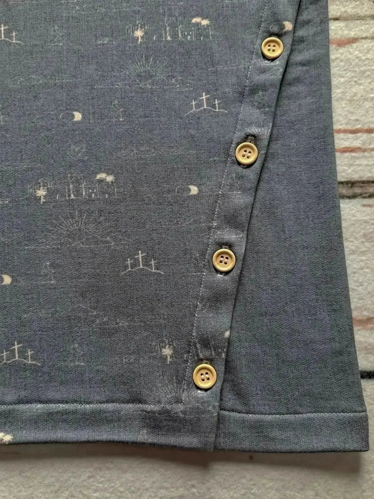 Gray fabric with subtle sky blue print of crosses and moons, featuring yellow buttons along the edge.