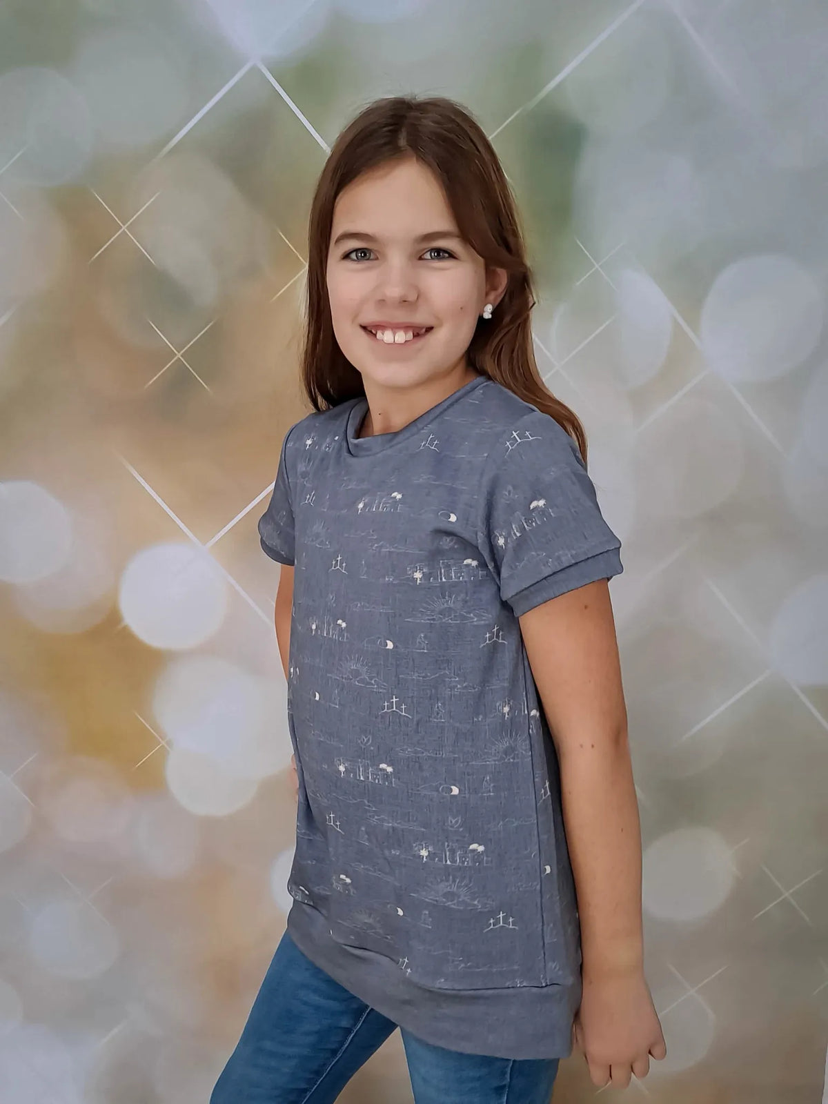 A young girl smiles, wearing a blue shirt with a subtle Resurrection Story pattern.