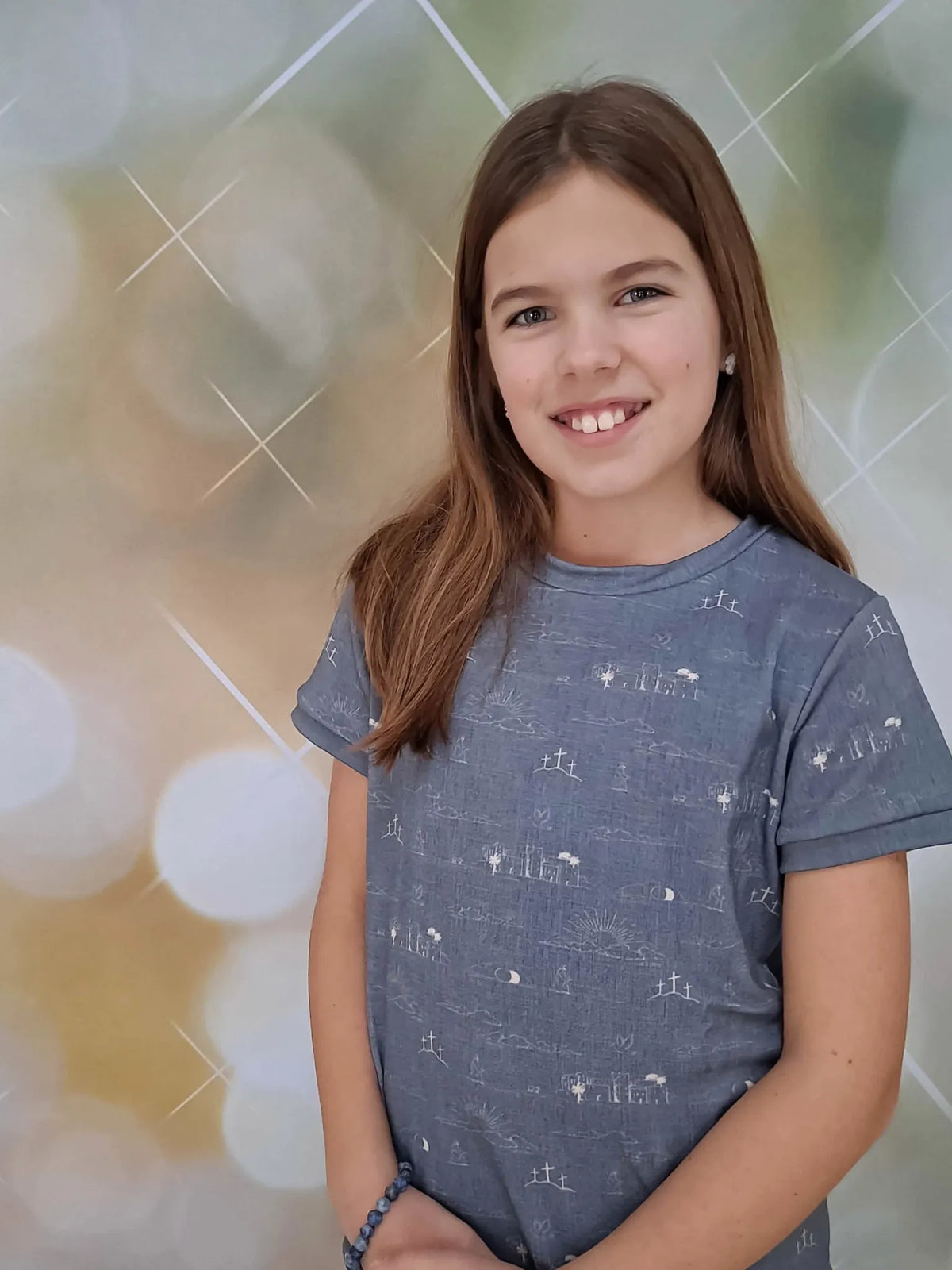 A young girl smiles, wearing a blue shirt with a Resurrection Story pattern.