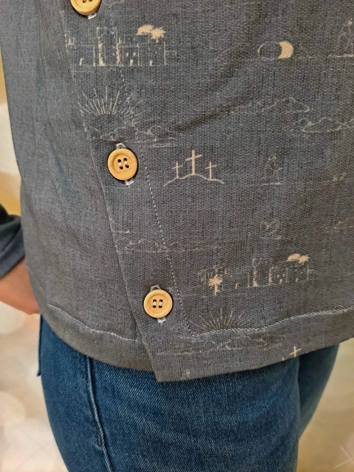 Gray fabric with subtle sky blue print of the Resurrection story, including crosses, palm trees, sun, and moon.