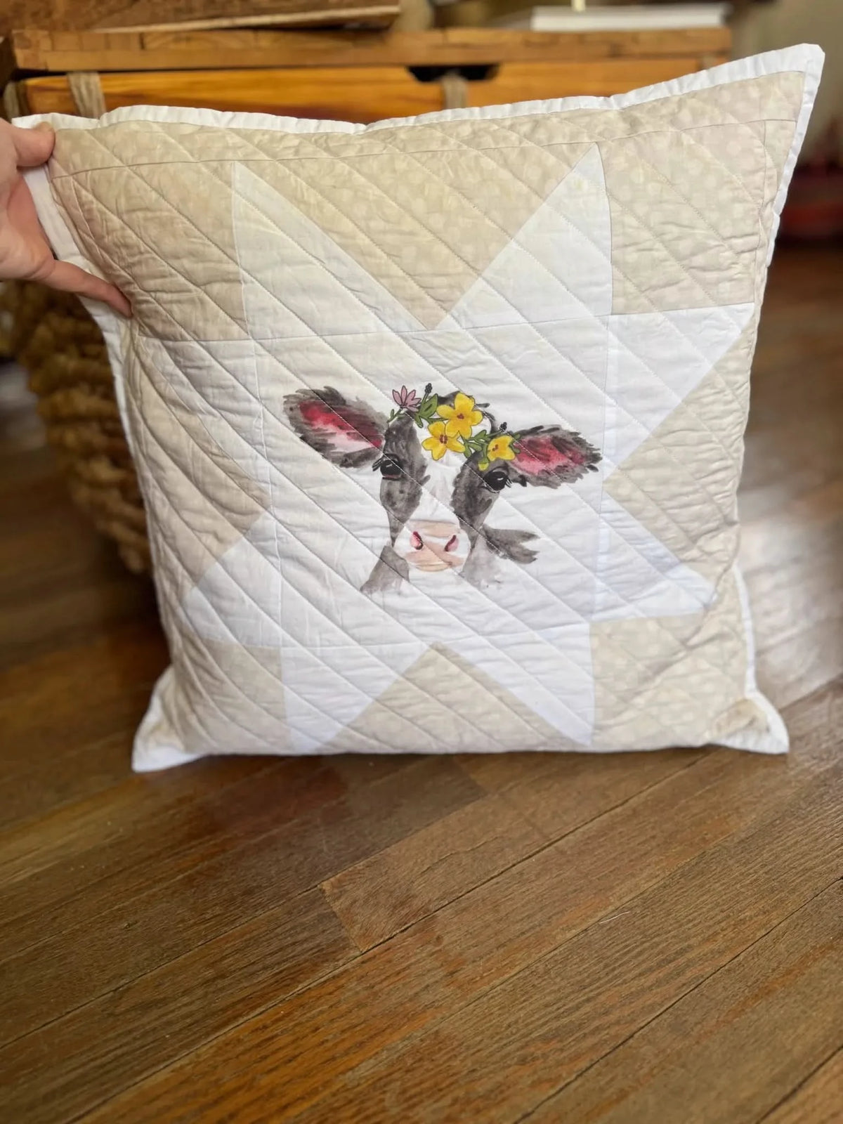A quilted pillow with a calf wearing a flower crown on a star pattern.