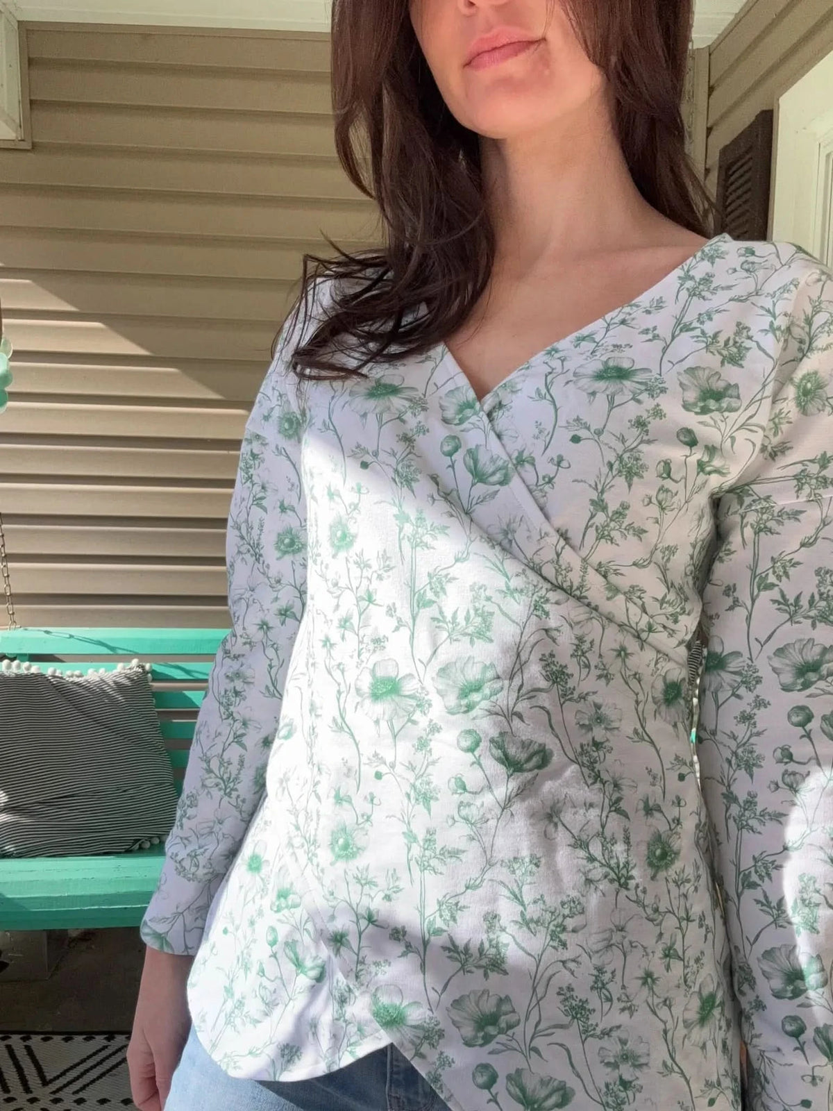 A woman wears a white wrap top with a green floral pattern.