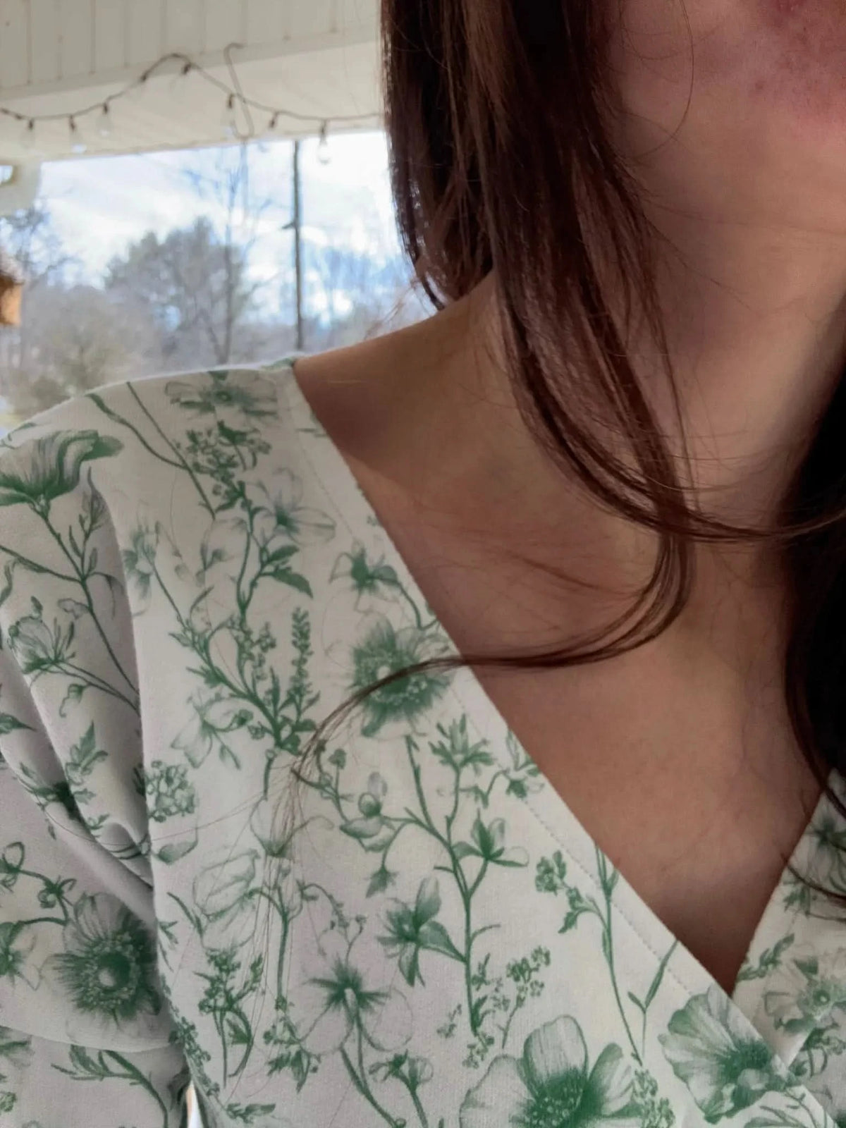 A person wearing a white top with a green floral pattern.