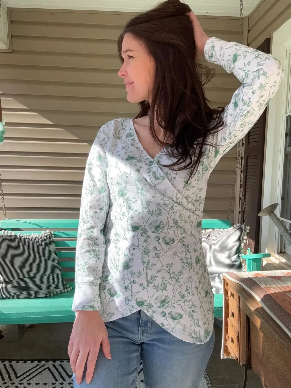 Woman wearing a green and white floral wrap top and blue jeans.