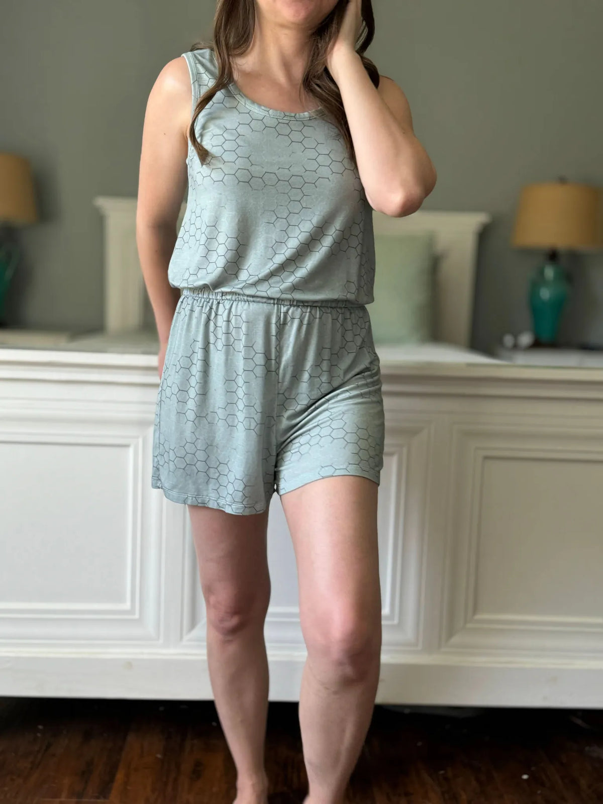 A woman models a light green honeycomb-patterned romper in a bedroom.