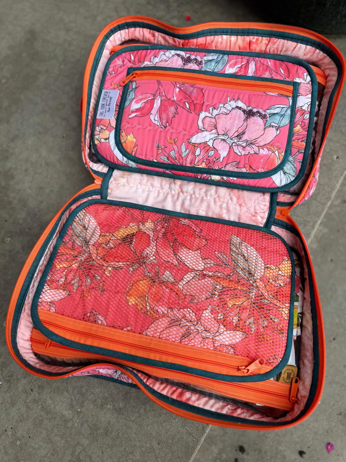 An open, coral-colored fabric organizer with floral patterns and mesh pockets.