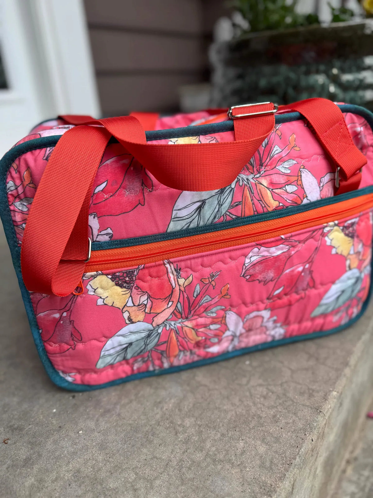 A quilted coral floral bag with a red strap and orange zipper.