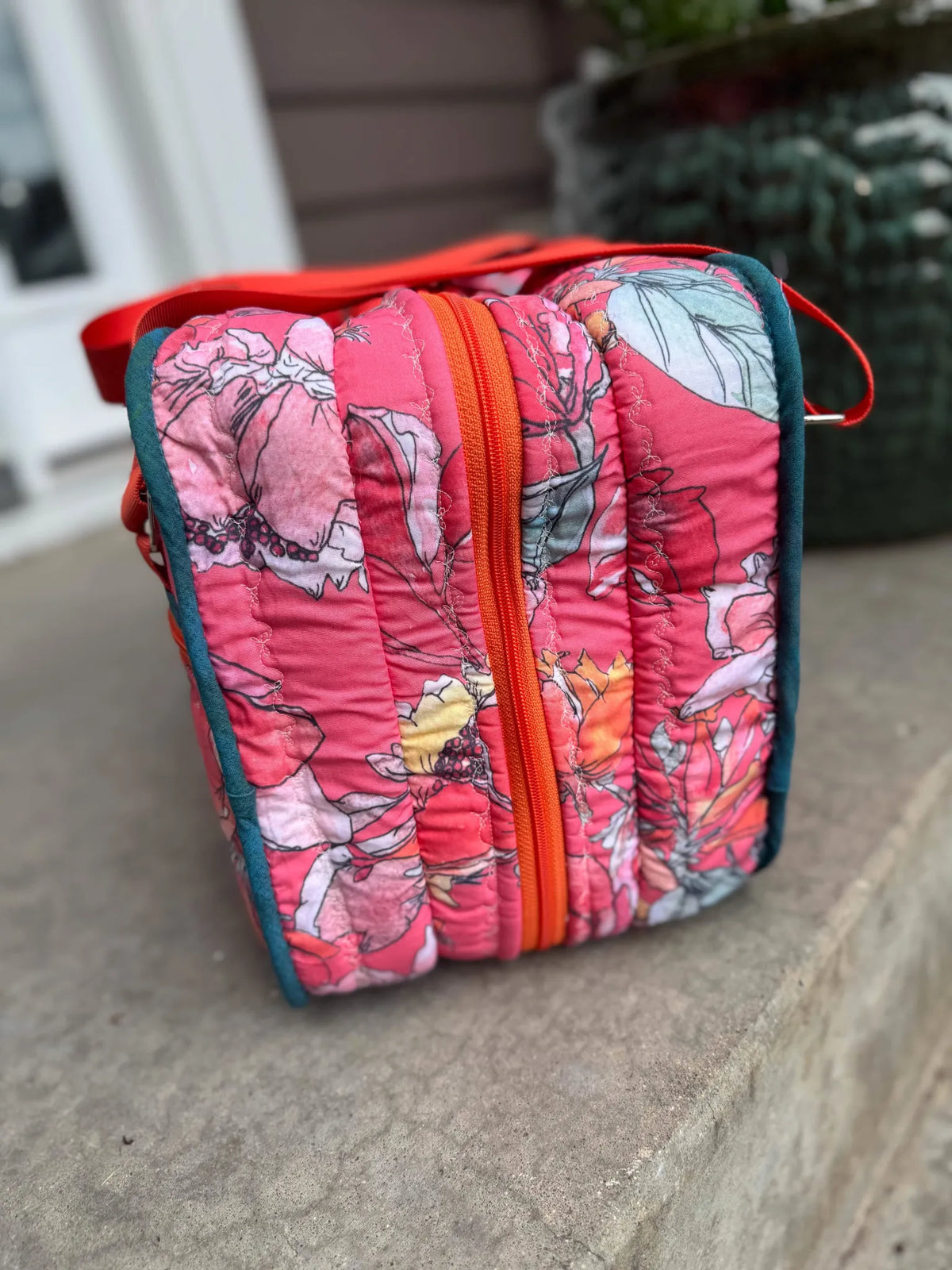 A quilted bag with a pink floral pattern, orange zipper, and teal piping.