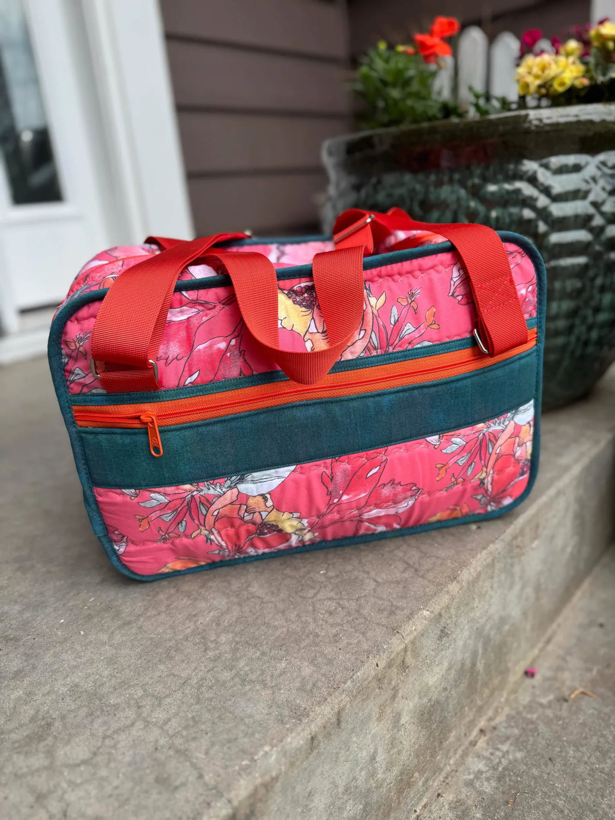 A quilted bag with a coral floral pattern, teal accents, and orange zippers.