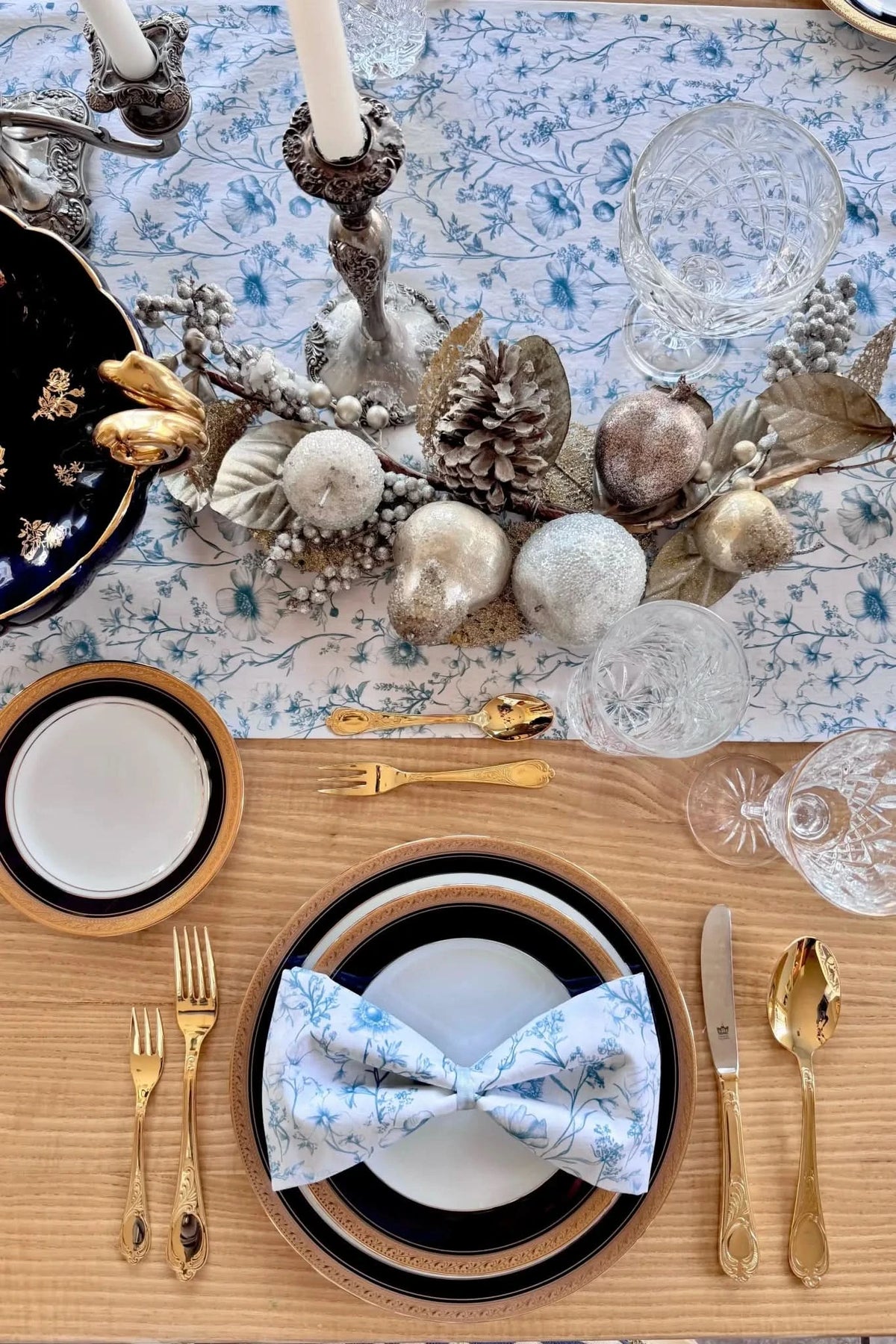 A table set with blue floral linens, gold flatware, and decorative accents.