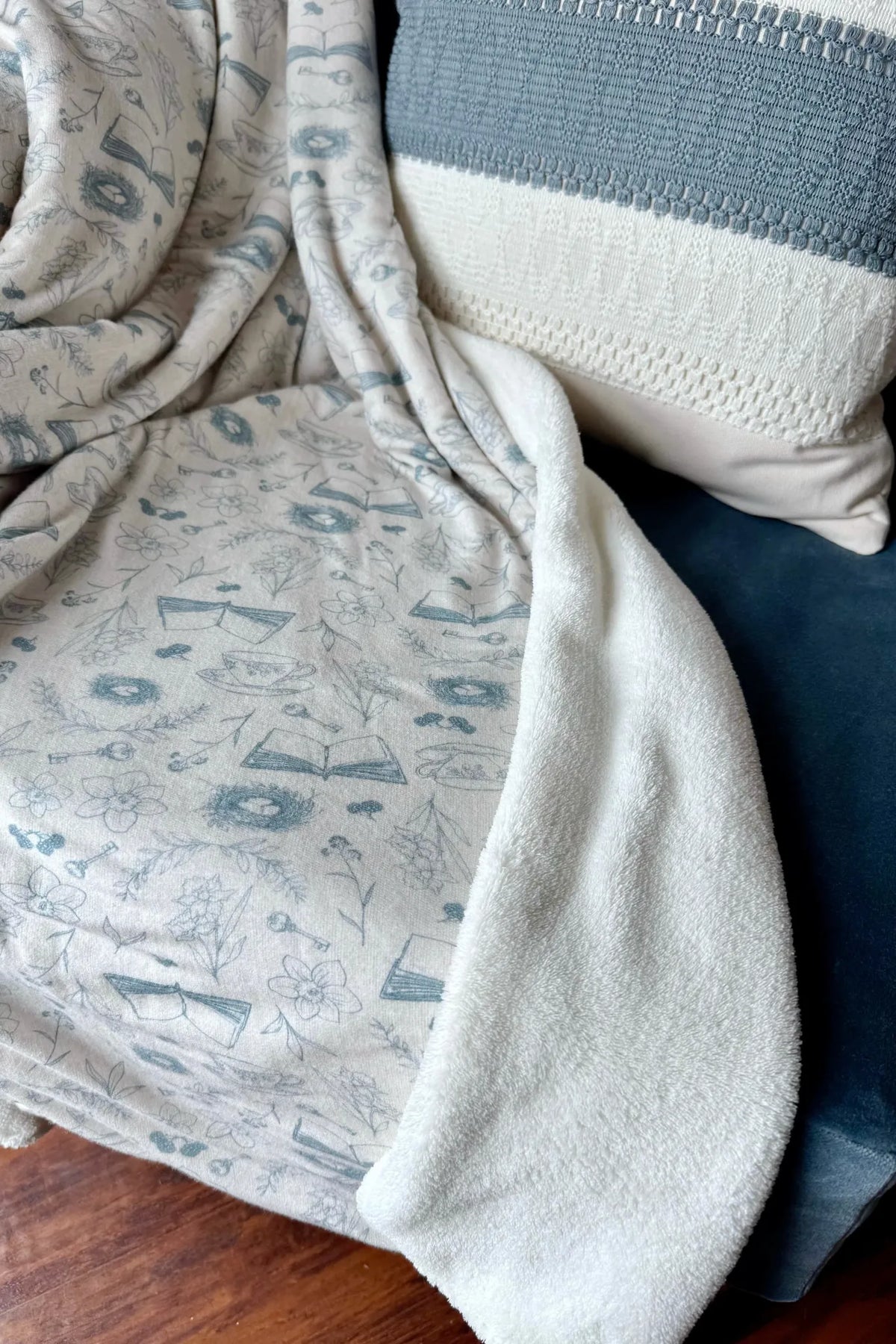 A white blanket with blue floral and book patterns, next to a striped pillow.