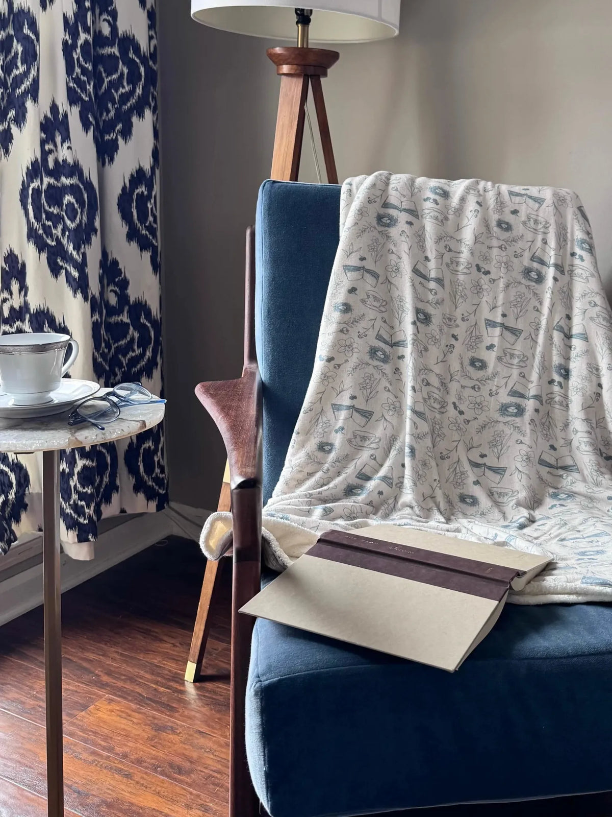 A white blanket with a blue tea and toile pattern draped over a blue chair.