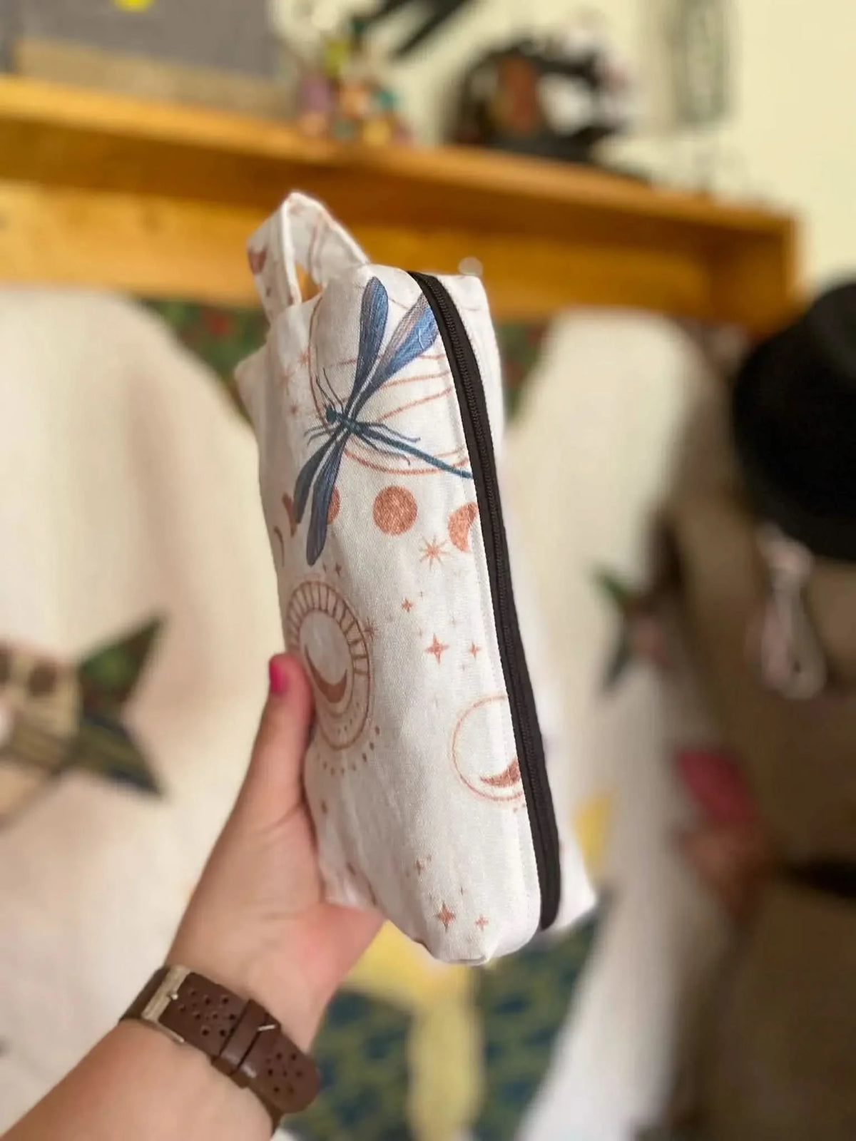 A white pouch with celestial dragonflies and moons, held by a hand.