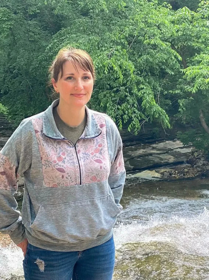 A woman wears a sage heather quarter-zip sweatshirt with a floral pattern.