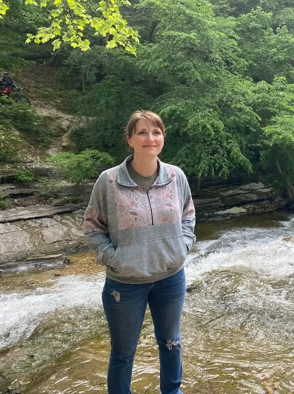 A woman wears a gray and pink floral quarter-zip sweatshirt and ripped blue jeans.