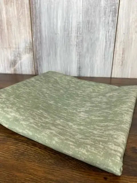 Sage green fabric with a subtle heathered pattern, folded on a wooden surface.