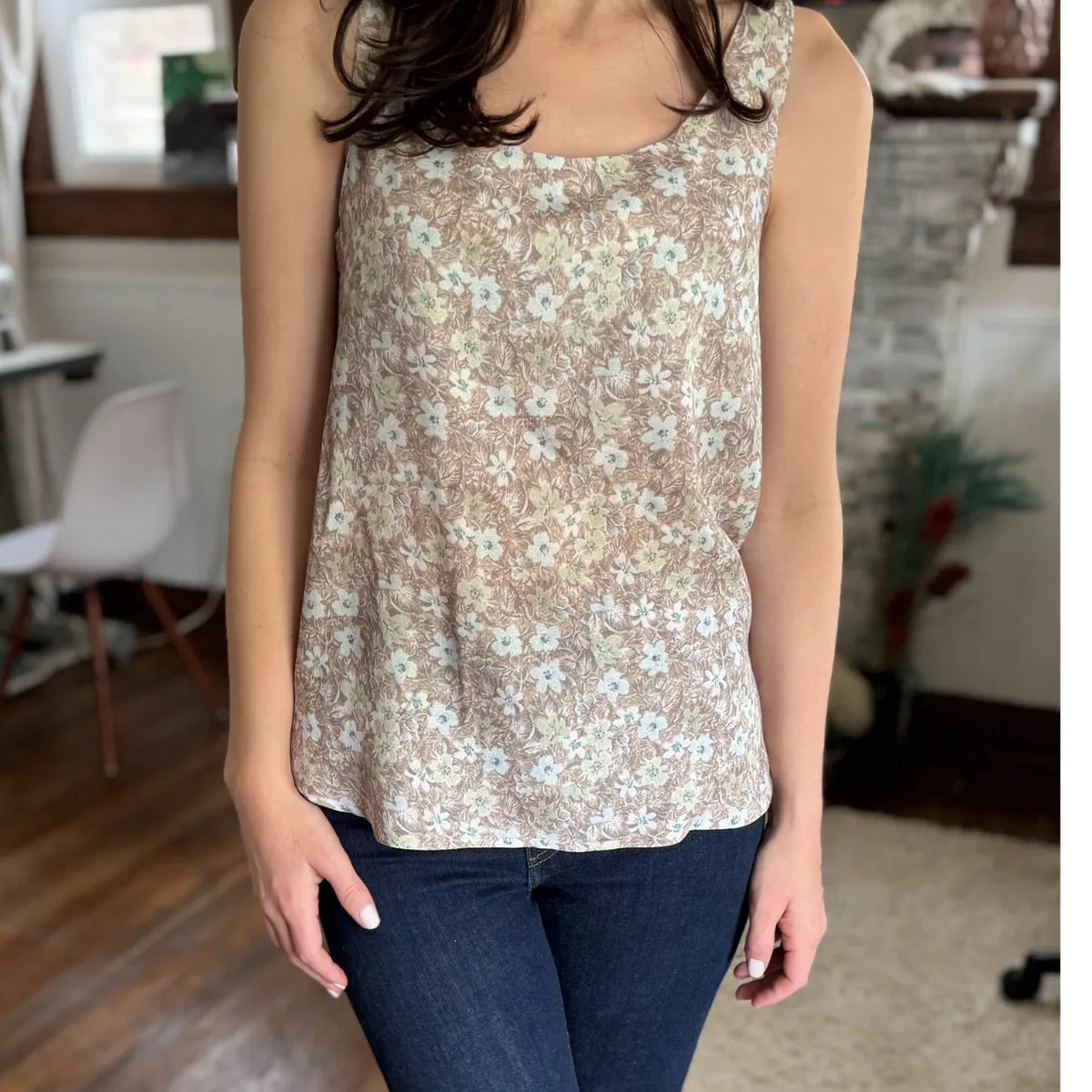 A woman wears a brown floral tank top and dark blue jeans.