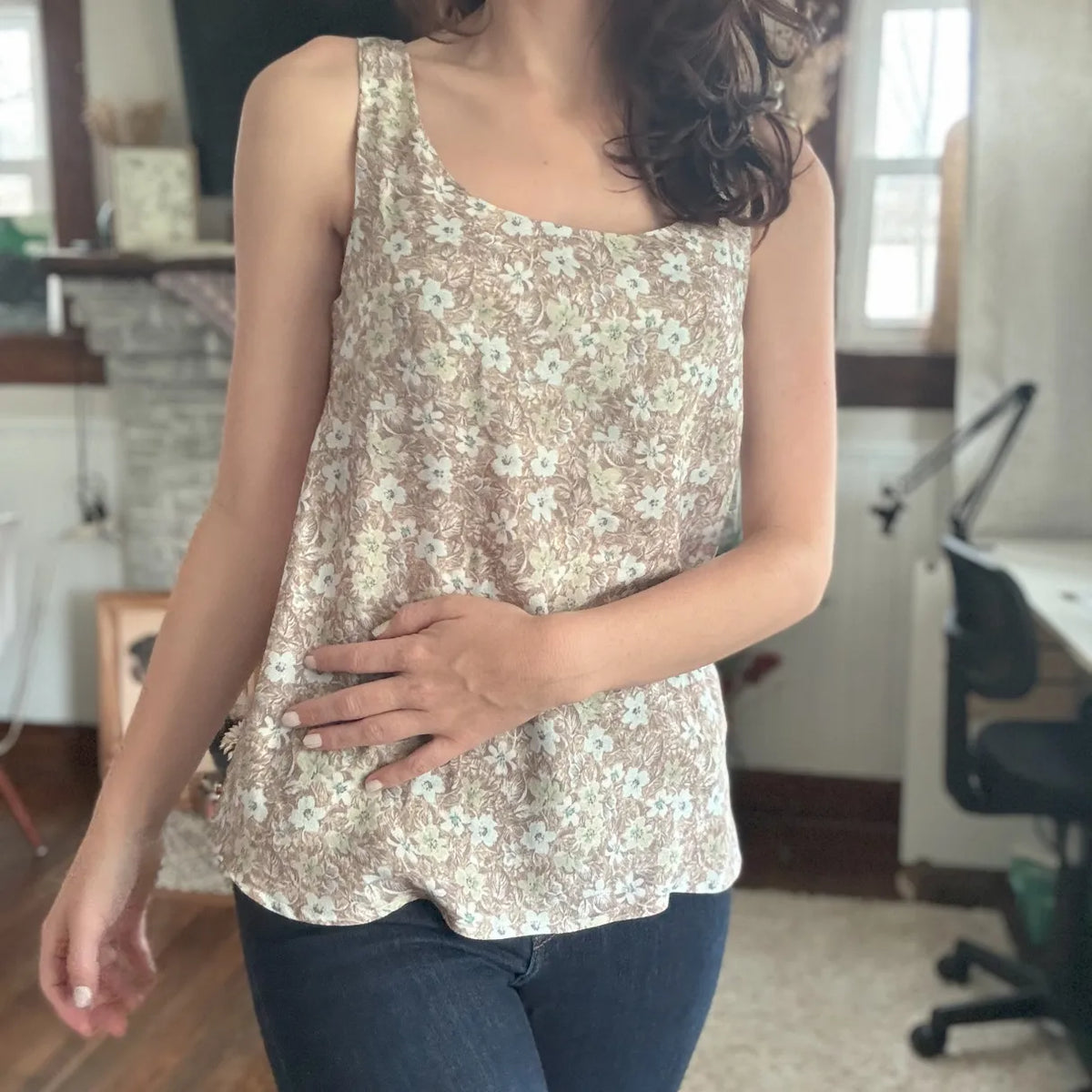 A person wears a brown wallpaper leaves print tank top with blue jeans.