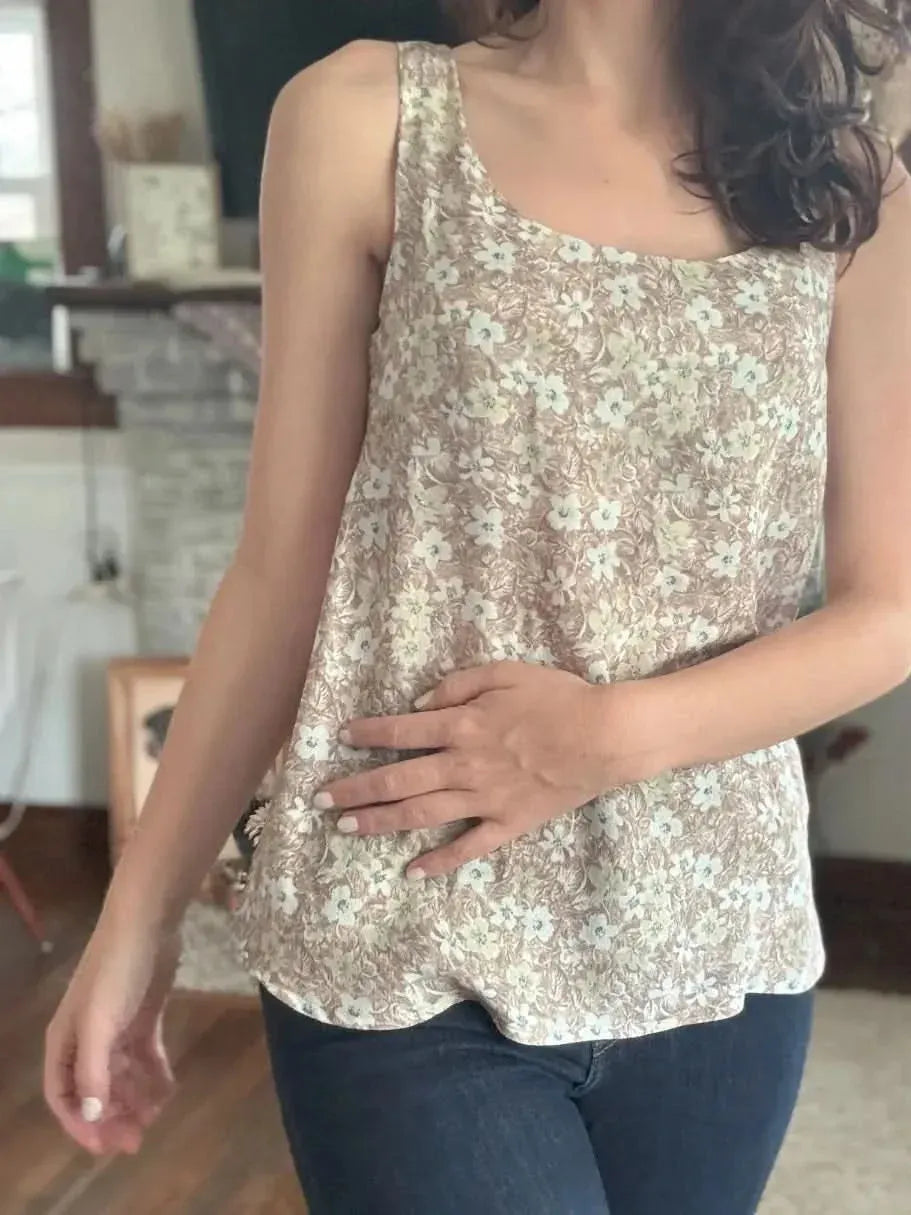 A person wears a brown wallpaper leaves print tank top with blue jeans.