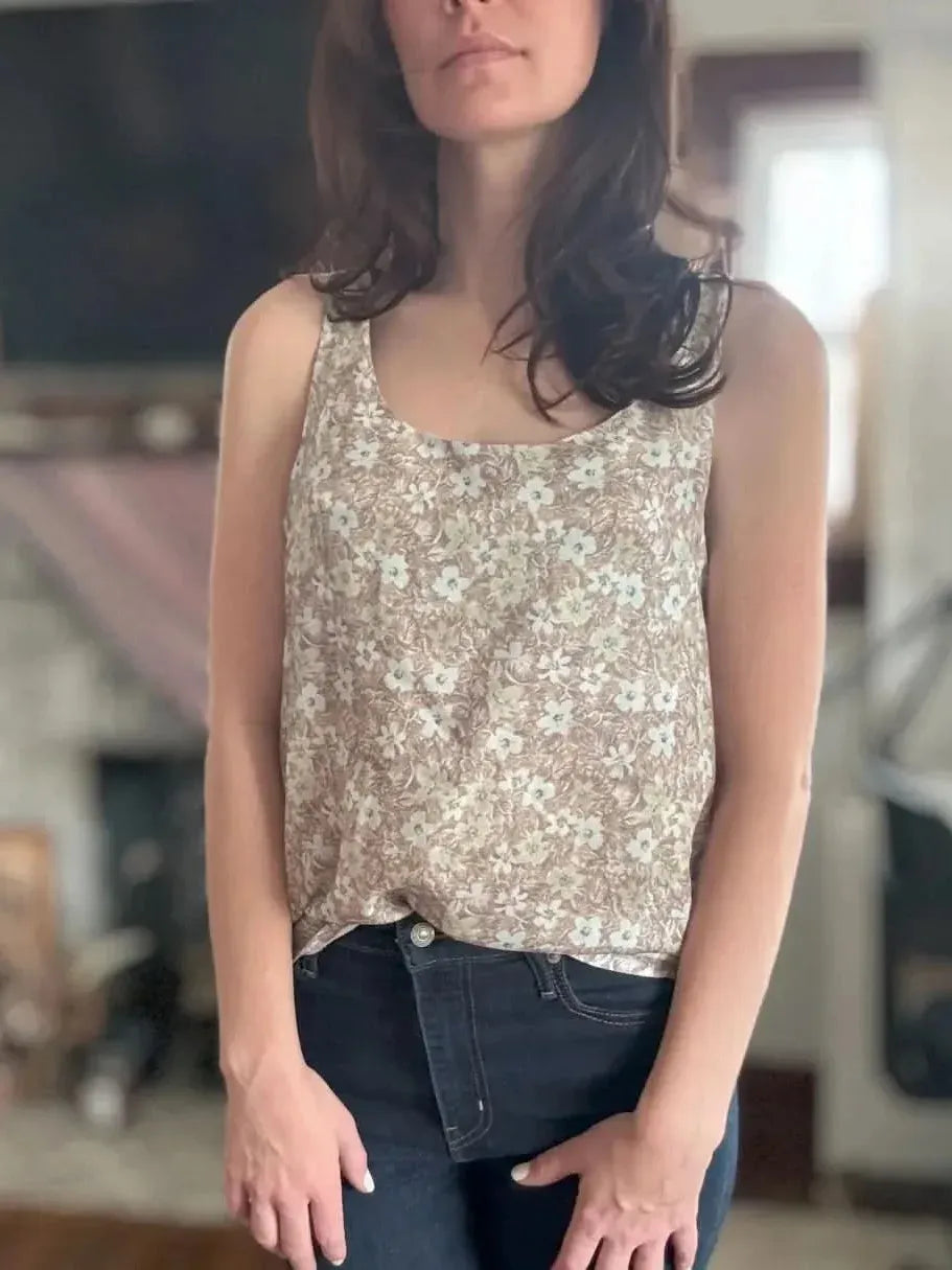 A woman wears a brown floral tank top and dark jeans.