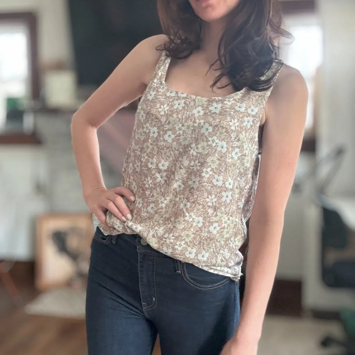 A woman wears a brown floral tank top and dark blue jeans.