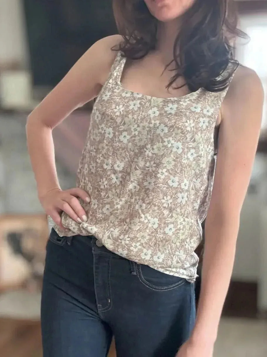 A woman wears a brown floral tank top and dark blue jeans.