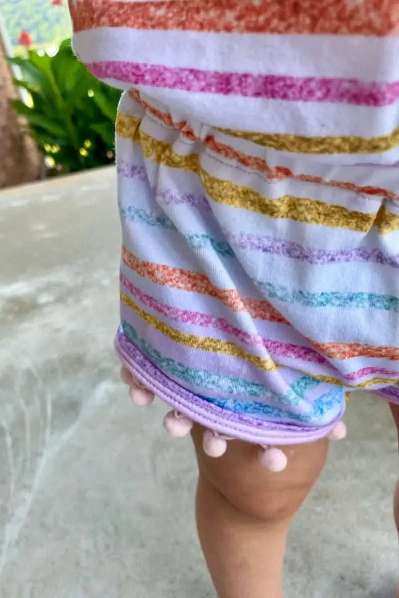 A close-up of a child's leg wearing a colorful striped garment with pink pom-poms.