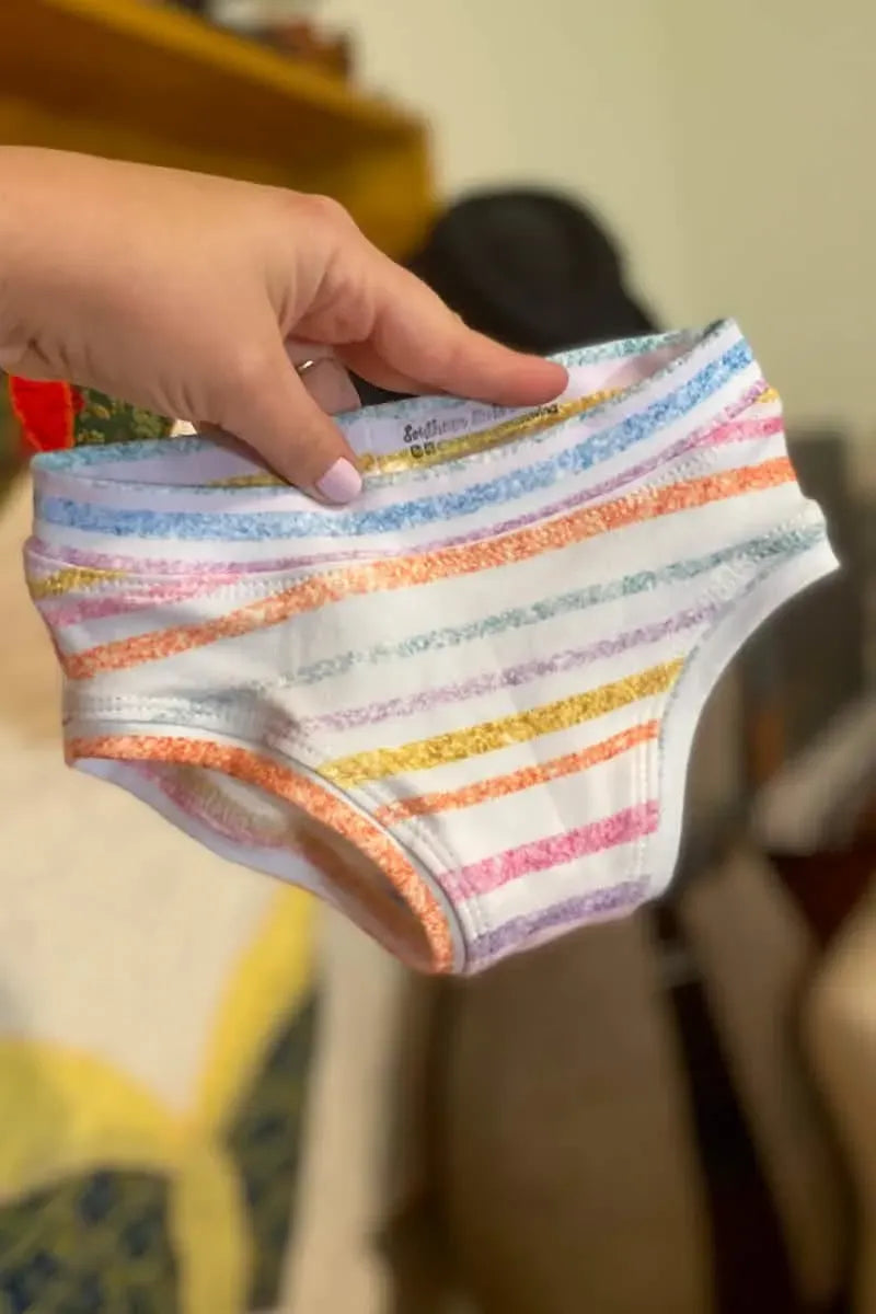 A hand holds up a pair of white underwear with colorful horizontal stripes.