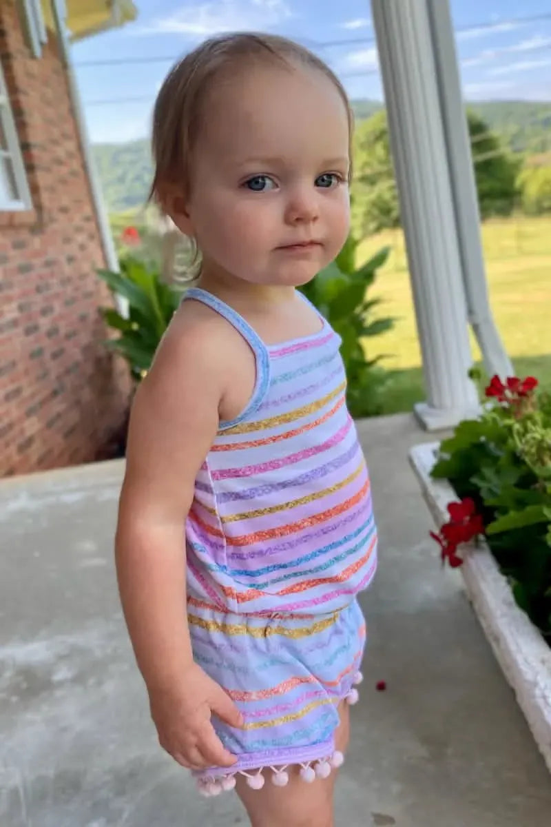 A young child wears a striped romper with pom-pom trim.