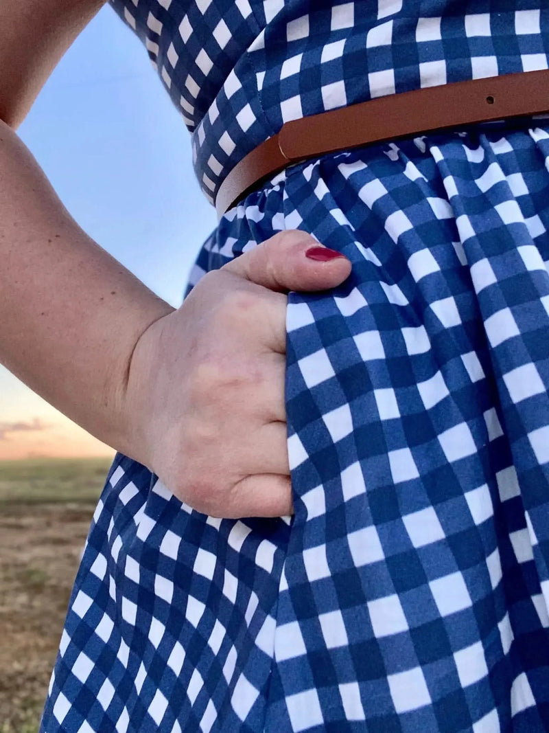 A person in a navy gingham dress with a brown belt and red nail polish.