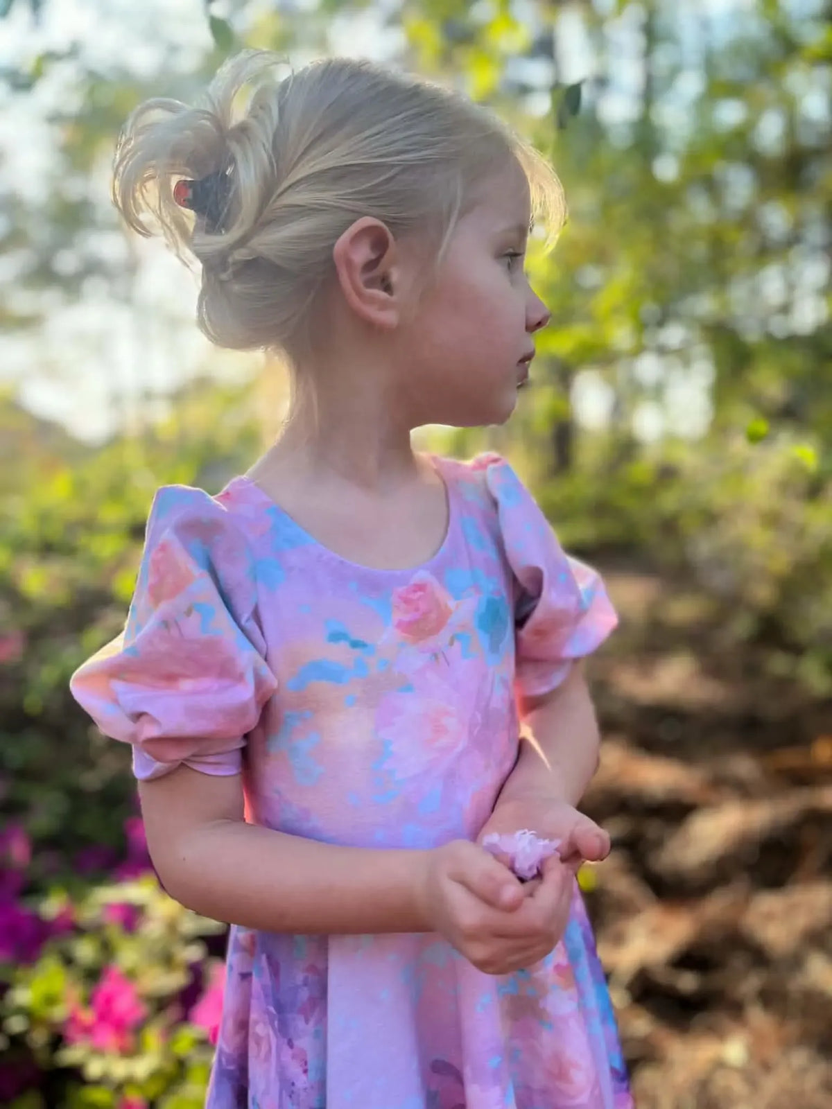 A young girl in a purple floral dress holds a flower petal.