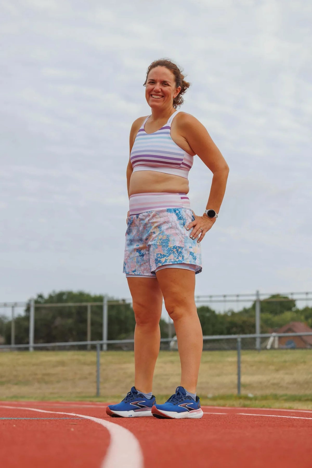 A woman in a striped sports bra and patterned shorts stands on a running track.