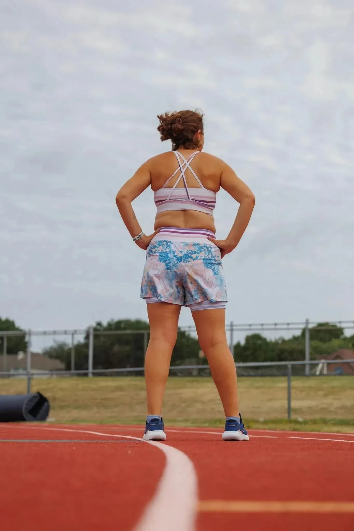A woman from behind on a track wears a striped sports bra and patterned shorts.