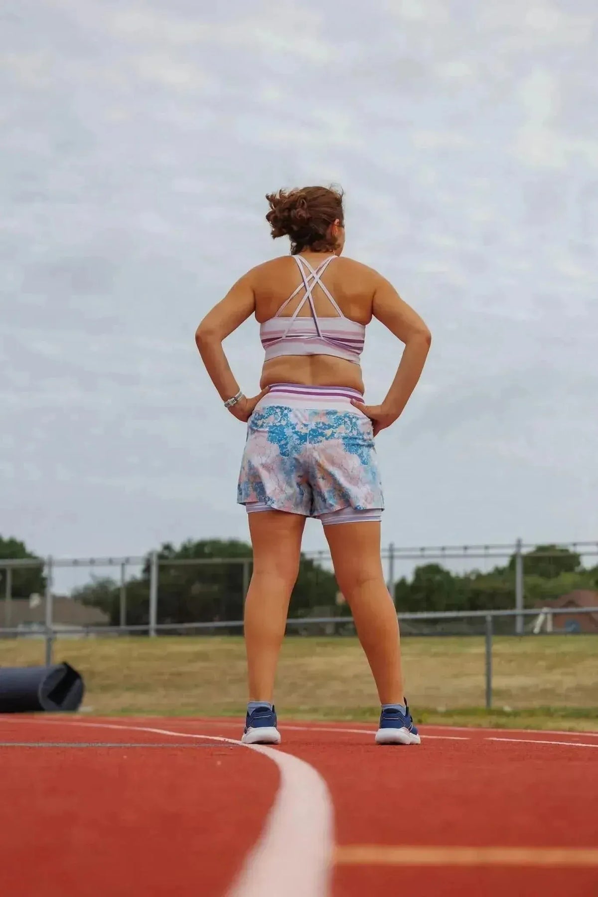Woman in back view wearing blue-pink abstract floral athletic shorts and sports bra on track.