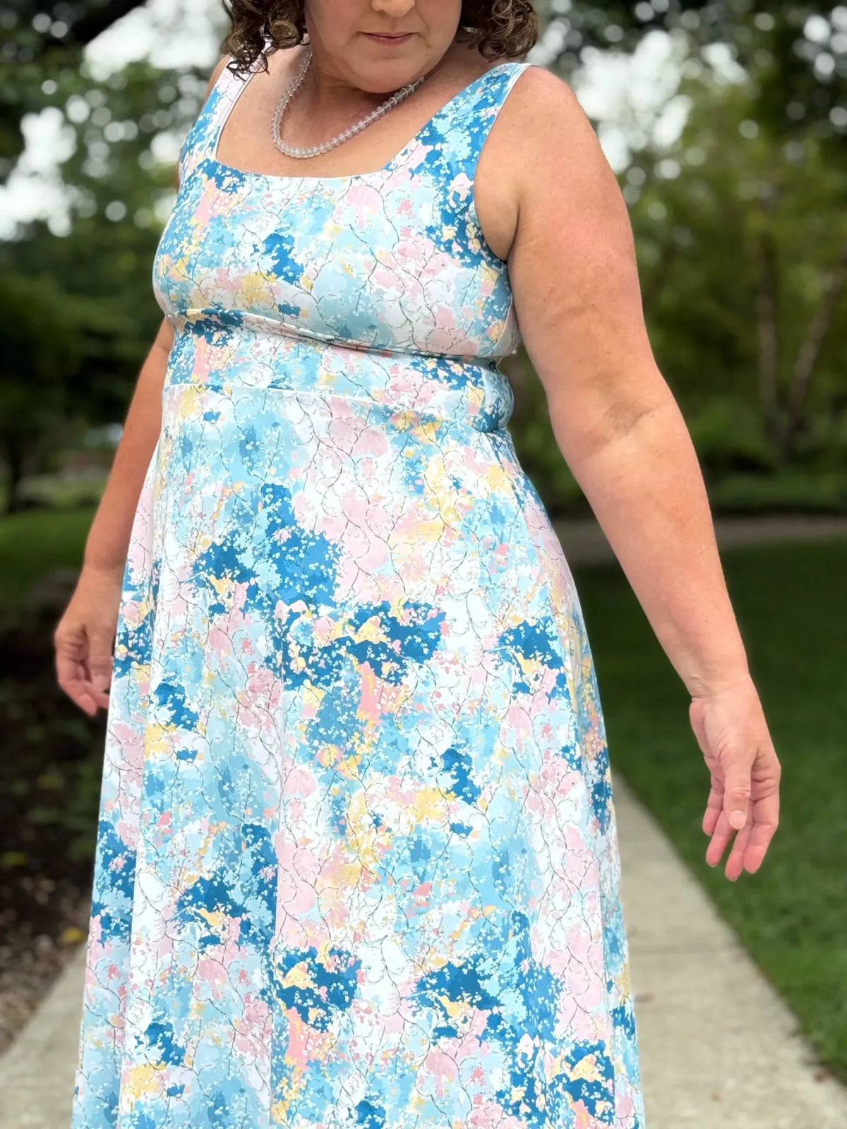 A woman wears a sleeveless dress with a blue, pink, and yellow floral pattern.