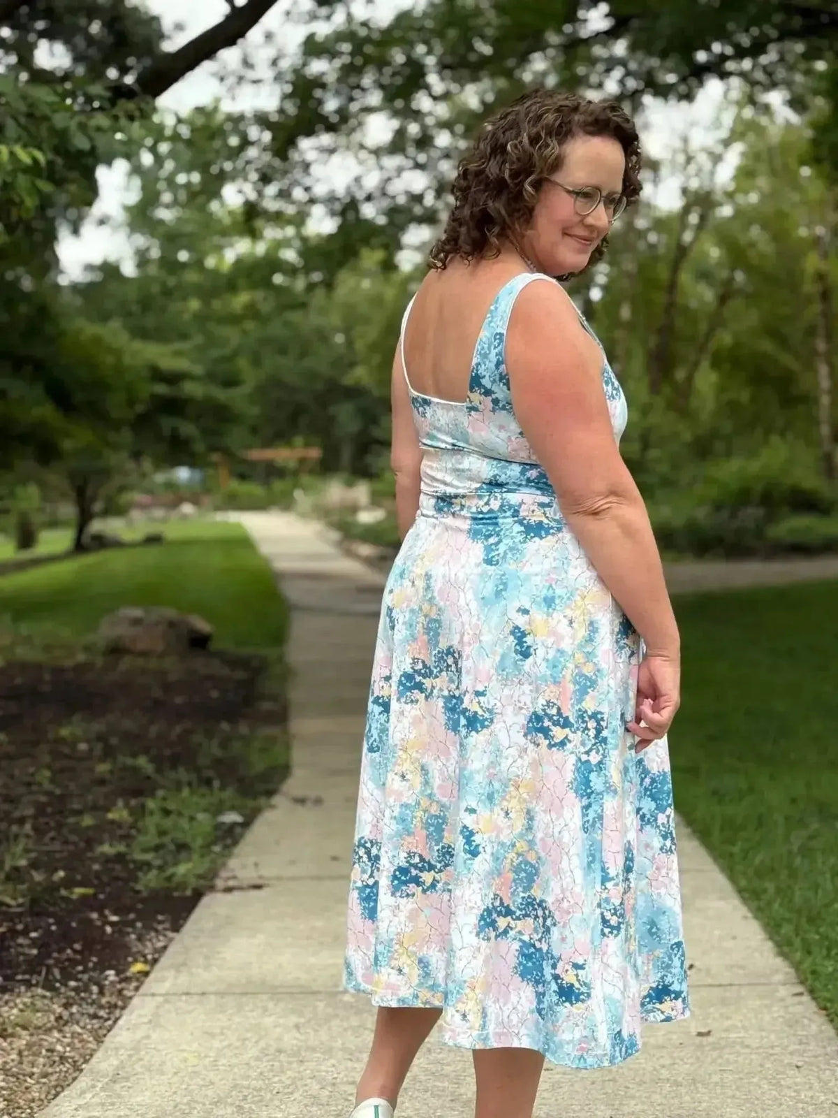 Woman wearing a sleeveless blue and pink abstract floral print dress in a park.