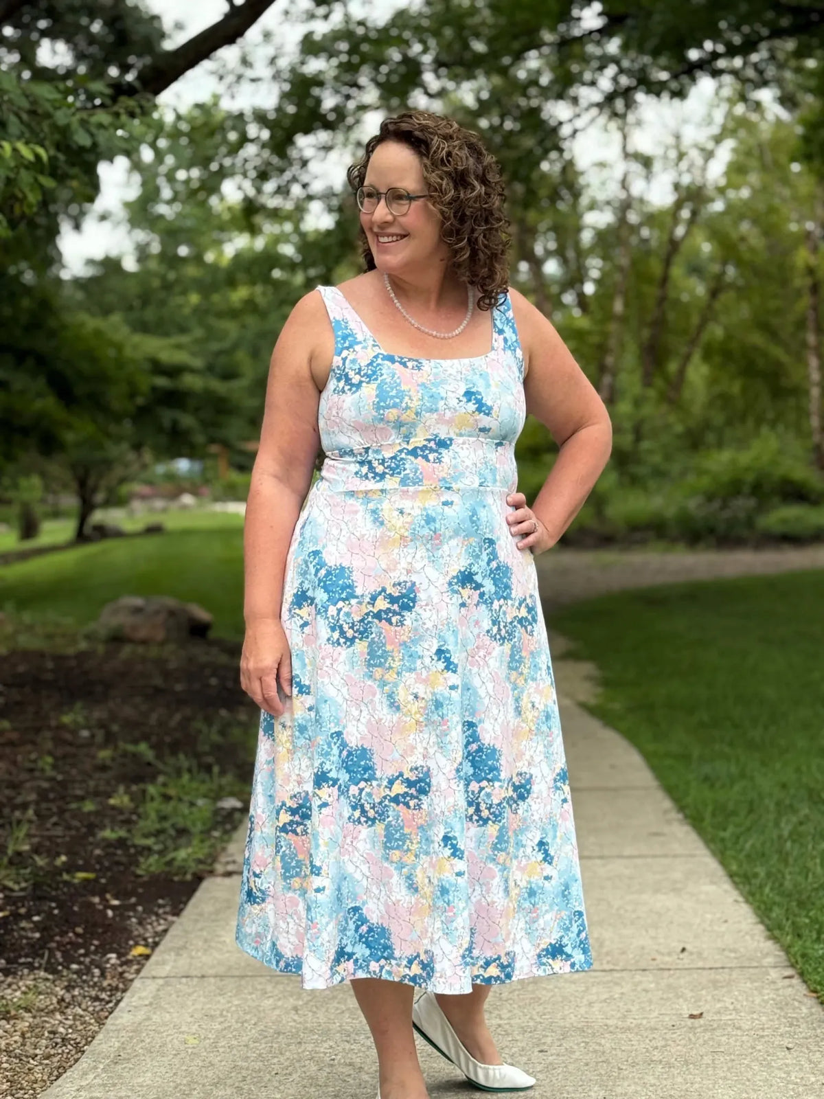 Woman in a blue, pink, and yellow floral dress with white flats.