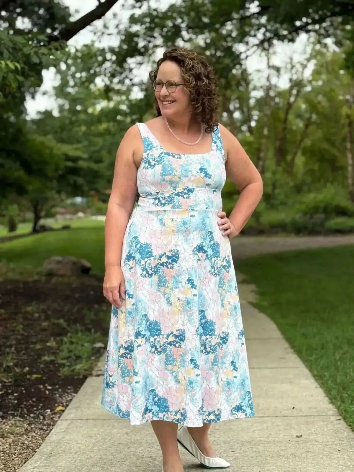Woman wearing a sleeveless midi dress in abstract blue and pink floral print, smiling outdoors.