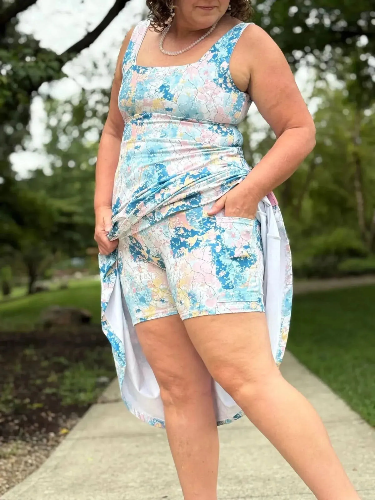 A woman wears a floral print dress with shorts underneath, posing outdoors.