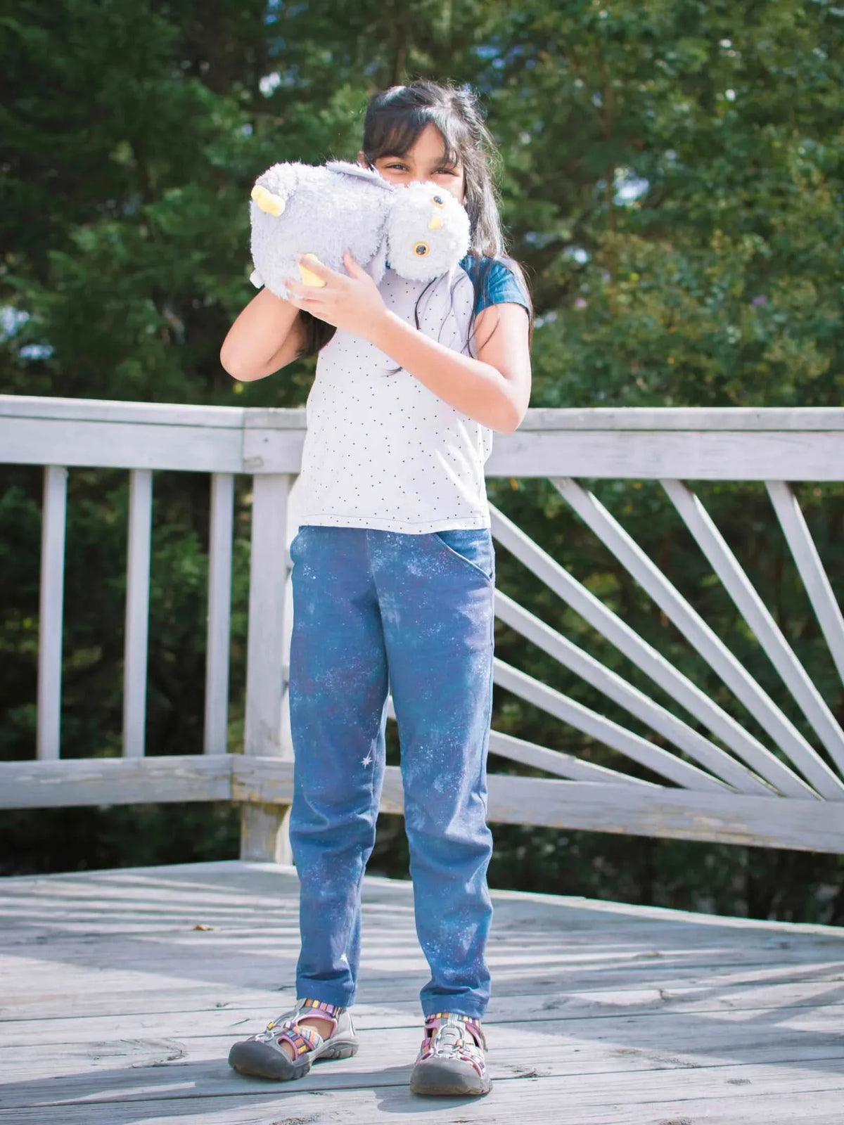 A young girl holds a plush toy in front of her face on a wooden deck.