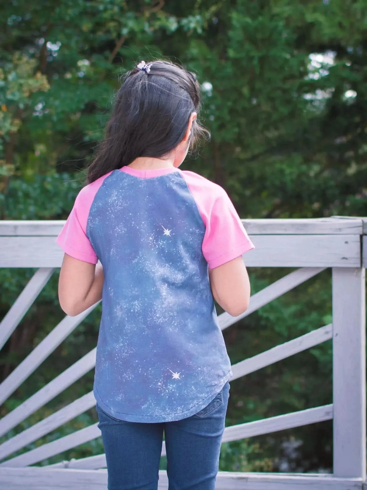 Rear view of girl wearing blue starry raglan t-shirt with pink sleeves outdoors.