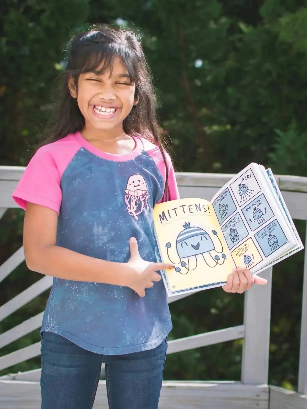 Girl wearing blue t-shirt with pink sleeves and jellyfish print, holding open Mitten book.