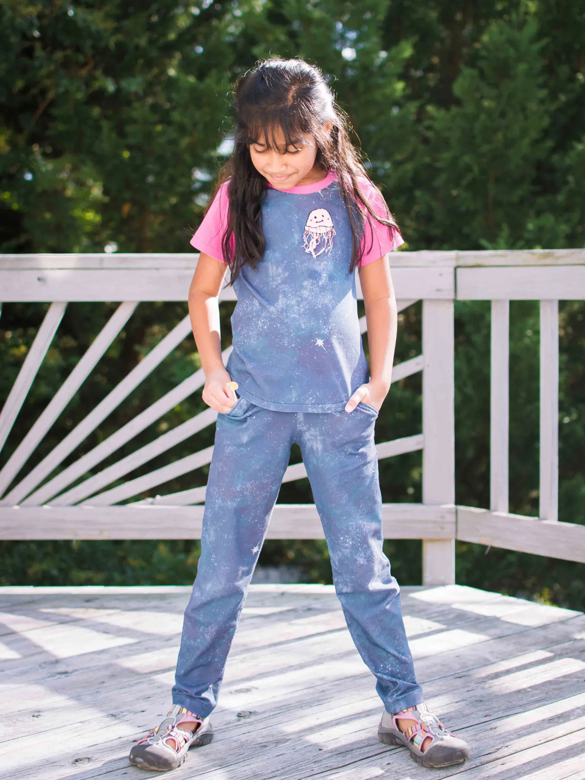 A young girl wears a blue and white galaxy-print shirt and pants with a jellyfish graphic.
