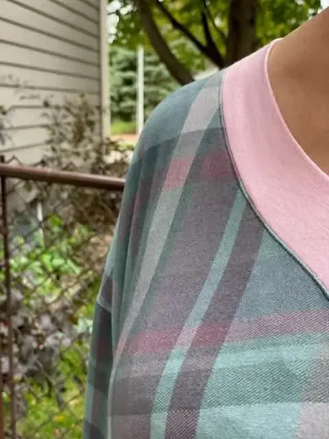 A person wears a plaid shirt with pink trim, featuring green, grey, and purple hues.