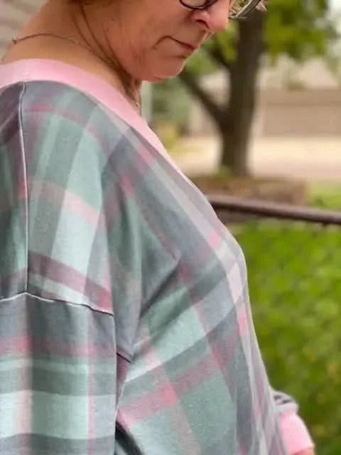 A person wears a pink and green plaid top with a silver necklace.