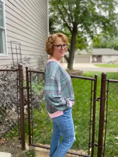A woman wears a plaid shirt with pink trim and blue jeans.