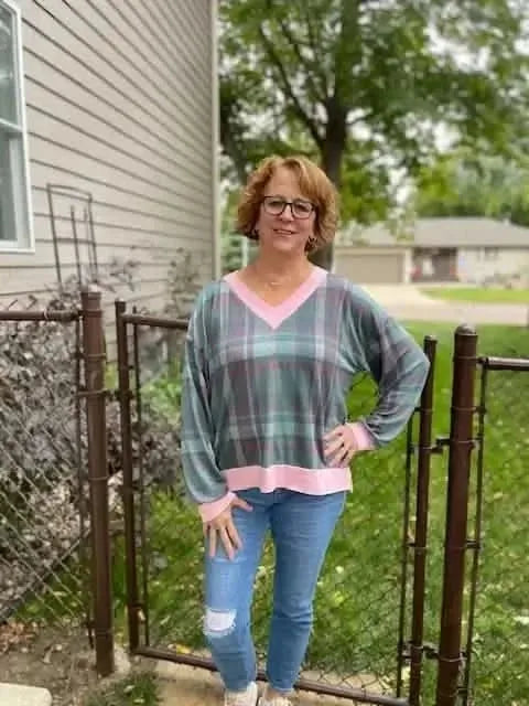 Woman wearing green and pink plaid V-neck top with bell sleeves outdoors.