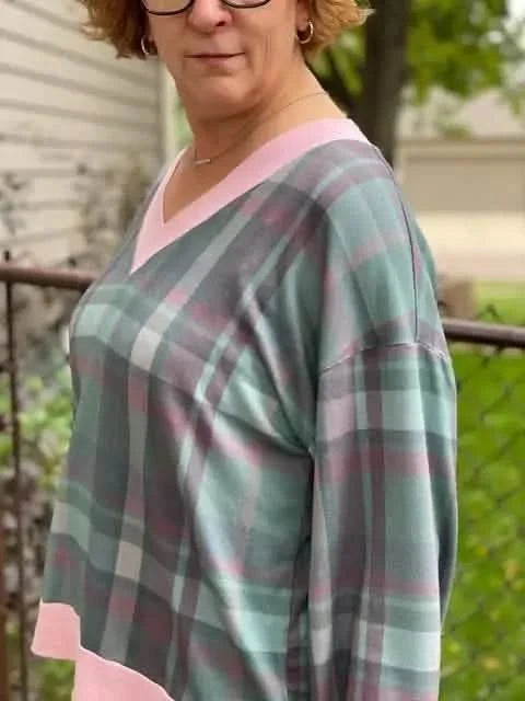 A woman wears a plaid shirt with pink trim, featuring shades of green, grey, and pink.
