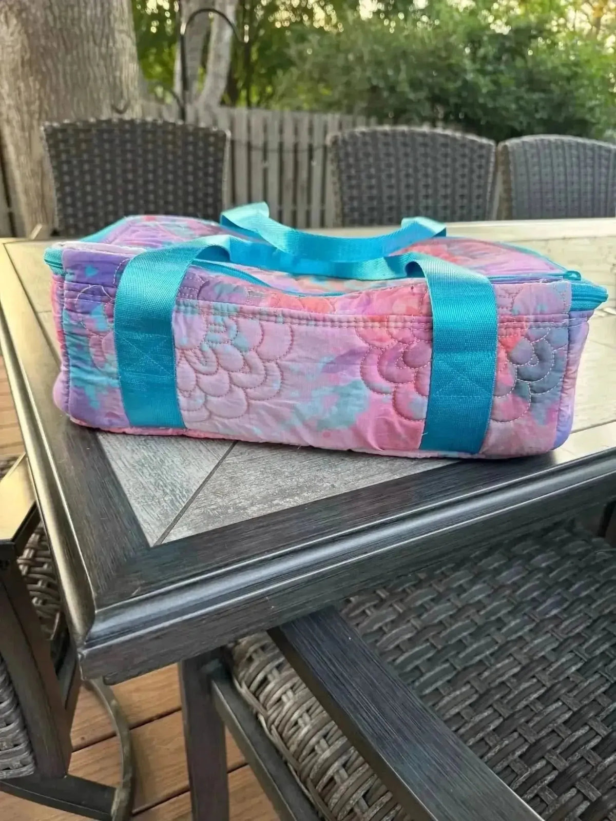 Purple glass flowers fabric with pink and blue accents, shown as a quilted bag on a patio table.
